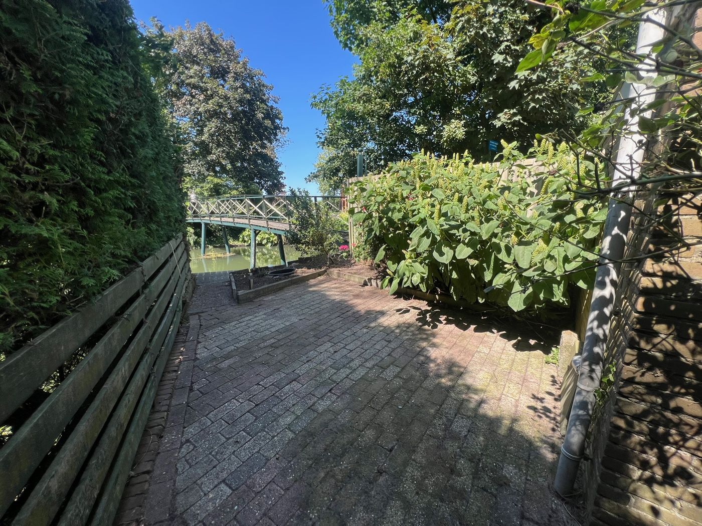 Dezelfde tuin na de klus: vrij pad met zicht op de brug en het water