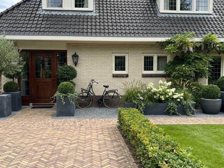 Impressie van een voortuin met grote antraciet plantenbakken, olijfboom en hortensia bij een vrijstaande villa