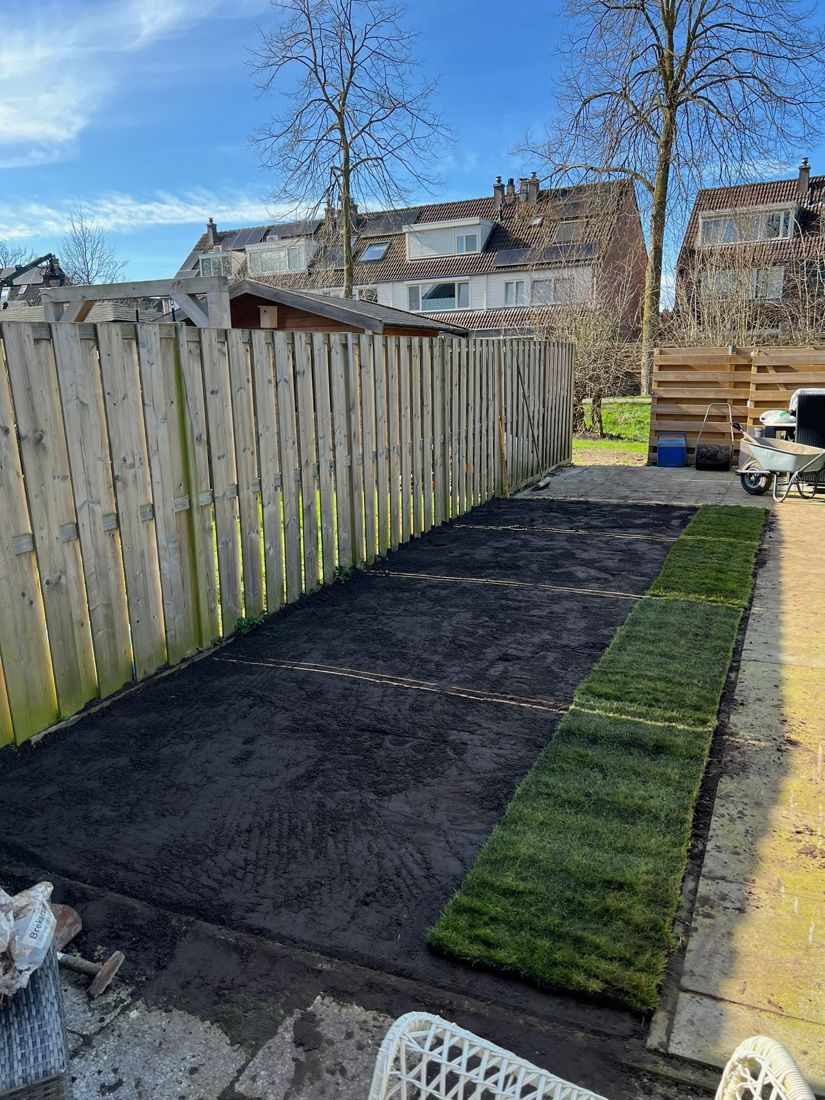 Grond geëgaliseerd langs de schutting, eerste rij graszoden ligt