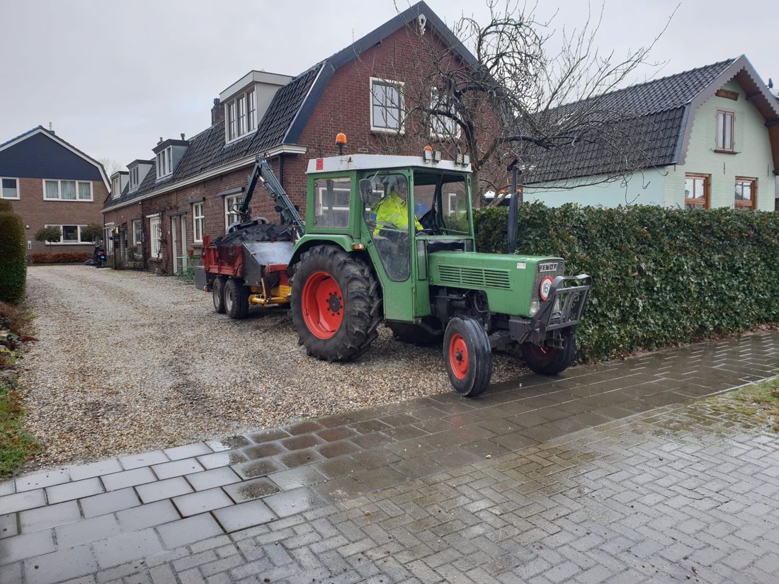 Tractor met kraanwagen en teamlid in geel werkjack op een grindoprit